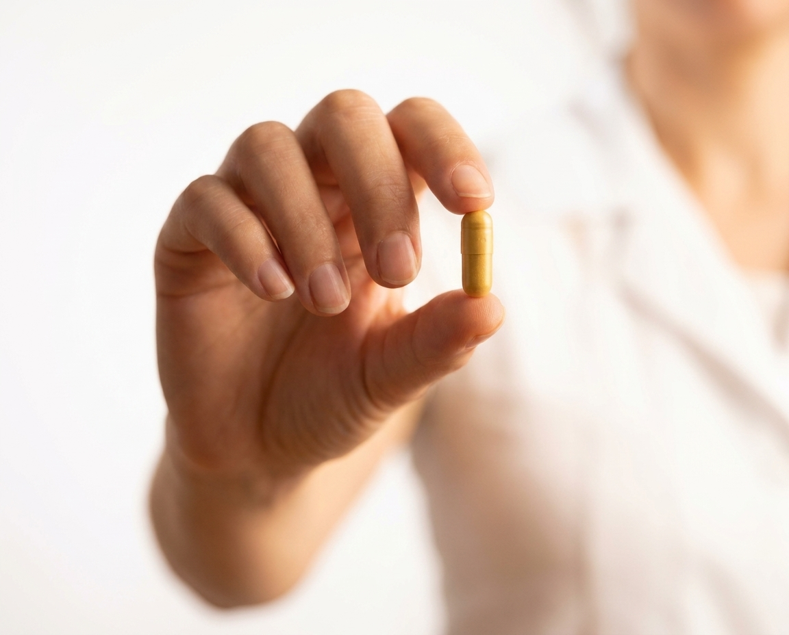 A hand holding a single naltrexone capsule